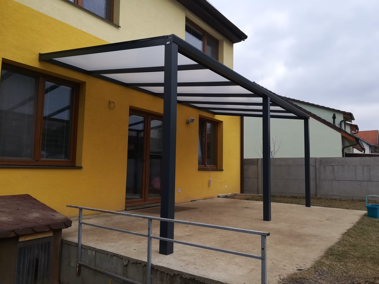 antracitová pergola ECO s opálovou střechou u žlutého domu