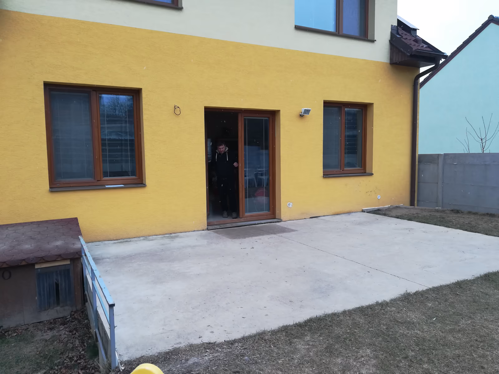 holá betonová deska u žlutého domu s hnědými dveřmi